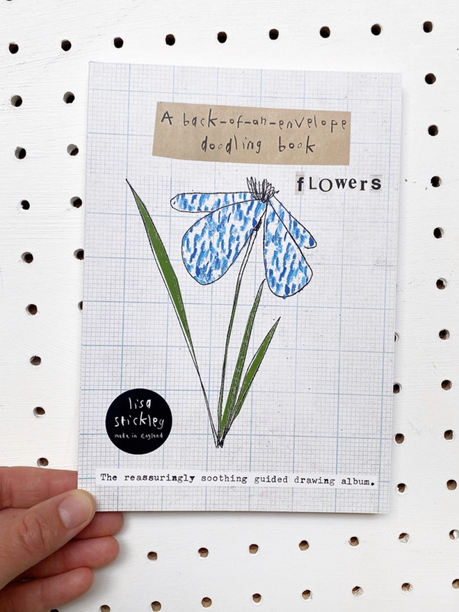 book with blue flower drawing on the cover on white peg board