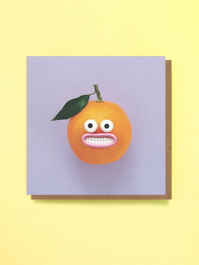 An Orange with a very smiley face, with a green leaf, on a Purple background 
