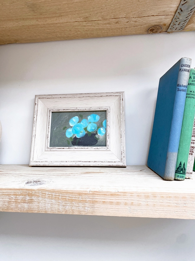 picture of shelf with framed picture of blue flowers and old books