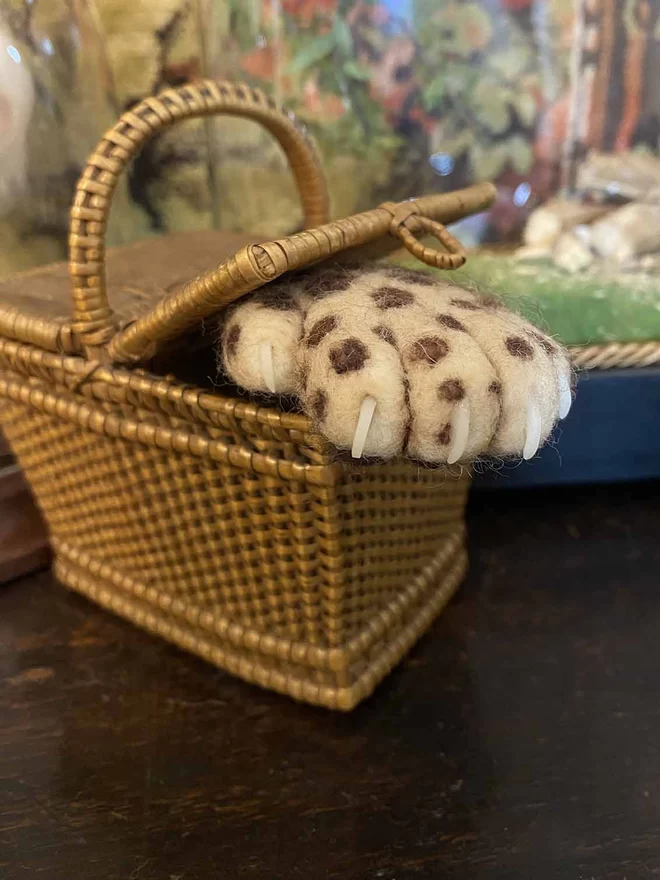 Needle-felted leopard paw brooch poking out of a miniature basket 