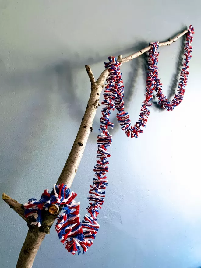 Red white and blue string tinsel looped on a branch against a dark grey wall