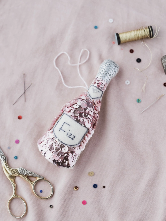 Pink sequinned champagne bottle ornament on a pink ground