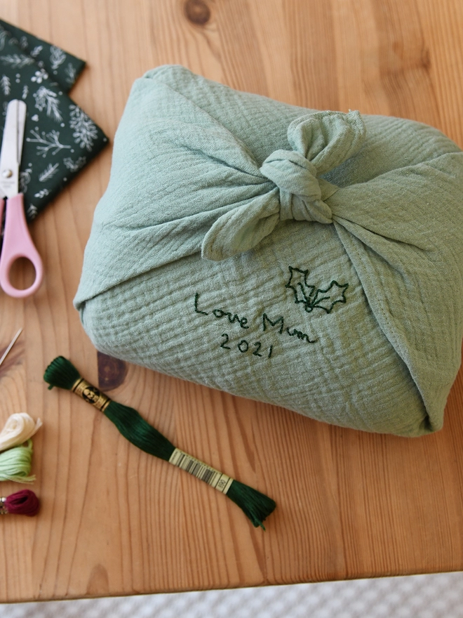 A gift wrapped in a mint green cotton fabric wrap that has been embroidered with a special message. 