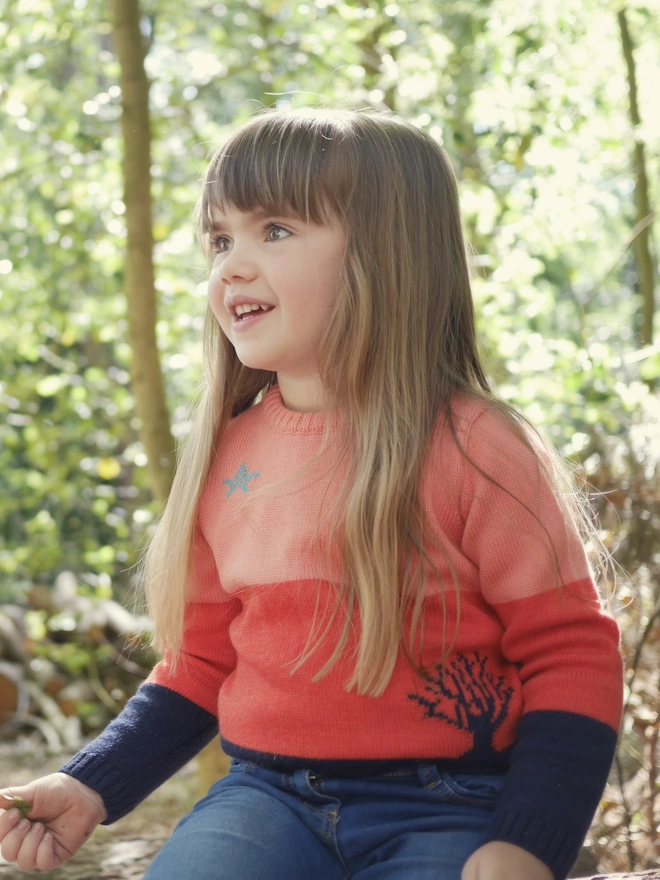 A little girl sat in the woods wearing 'The Stargazer' Jumper by The Faraway Gang.