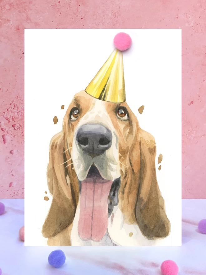 Basset Hound Pompom Birthday Celebration Collection Card in front of a pink background and surrounded by pompoms