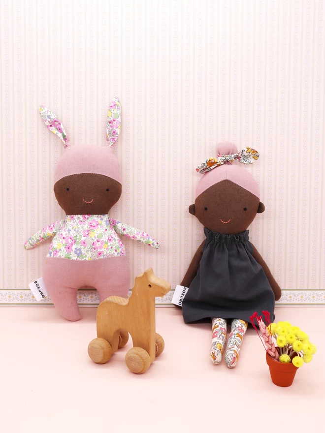 textile doll with dark skin and pink hair next to pink bunny doll