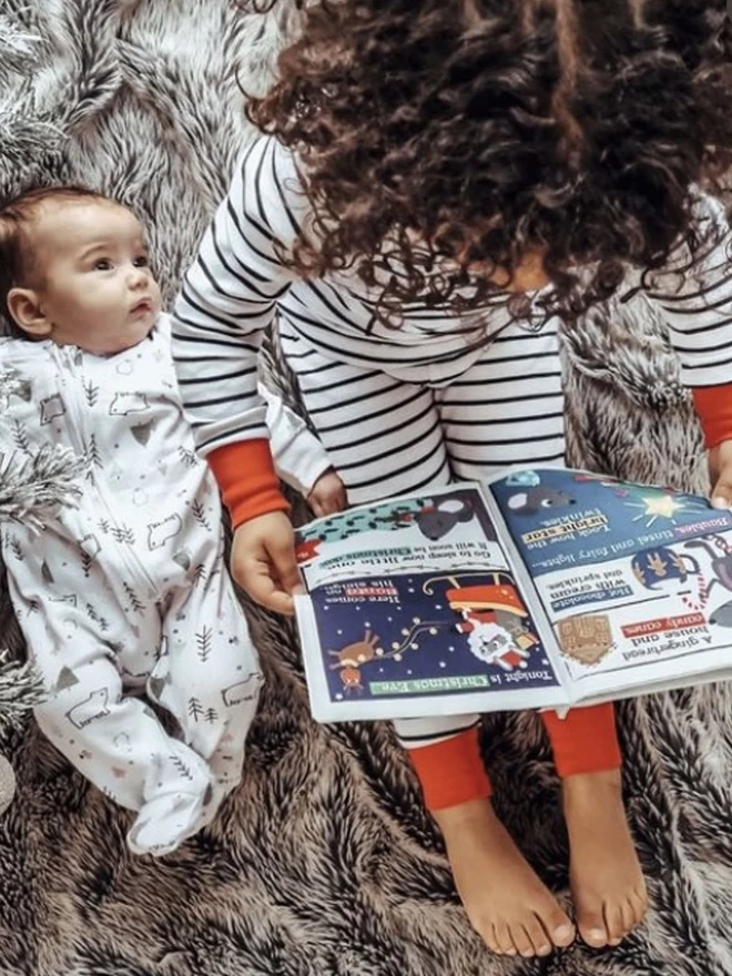 Toddler reading Christmas is here Newspaper with newborn besidee, view from above