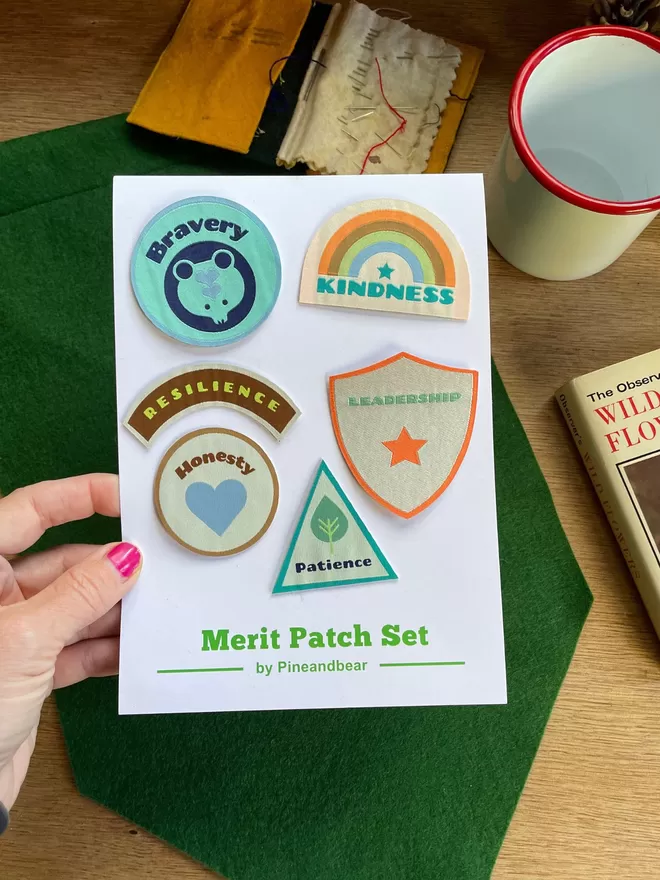 A hand holding the merit patch set with 6 patches on a white presentation card.