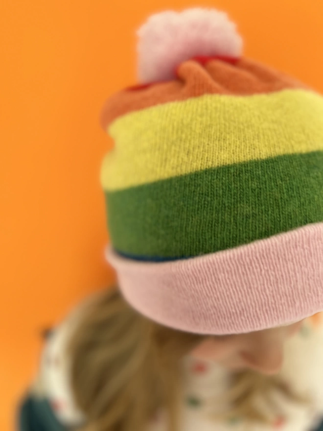 Rainbow striped knitted beanie hat being worn by 5 year old girl