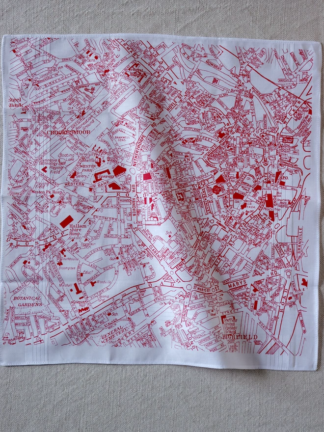 A Mr.PS Sheffield map hankie printed in red laid flat on a linen tablecloth