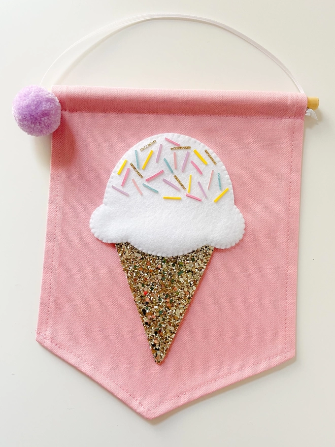 A white ice cream with a gold glitter cone on a pink banner