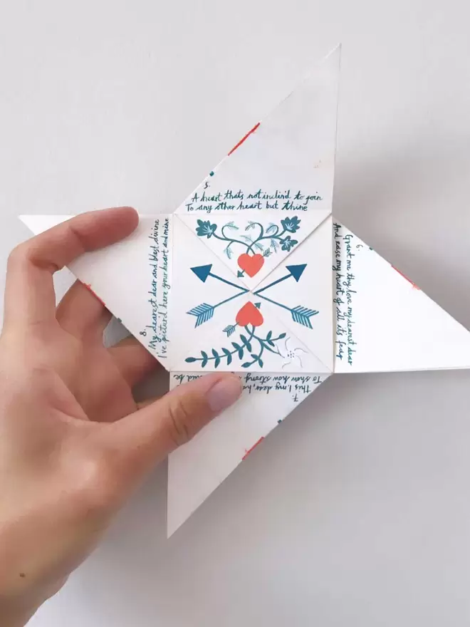 An origami love letter is half open in Fiona's hand, some of the poem is visible