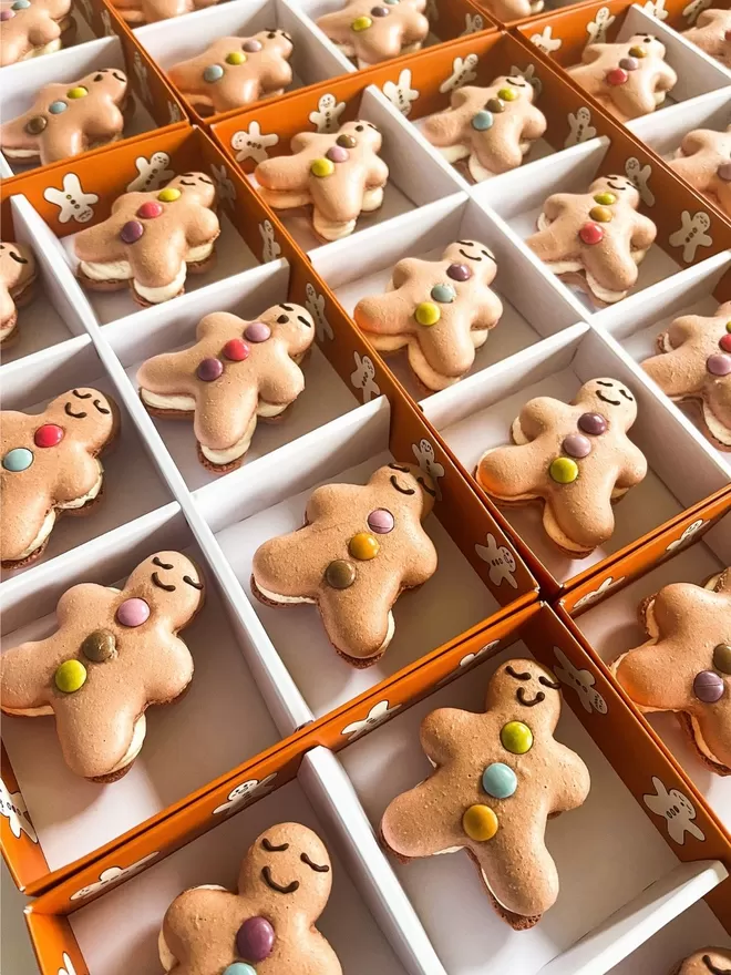 several gingerbread men macarons are arranged in an orange box decorated with gingerbread men cartoons