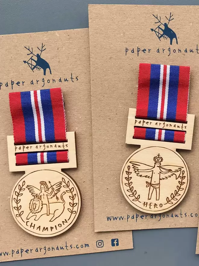 Two wooden medal pin badges are shown, engraved with 'Champion' and 'Hero', on blue and red ribbon