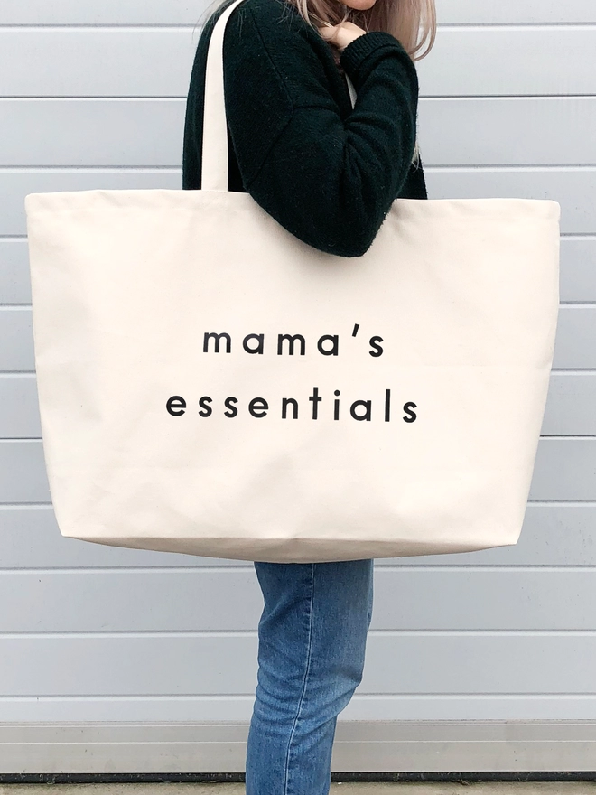 model carrying a oversized natural canvas tote bag with mama's essentials slogan