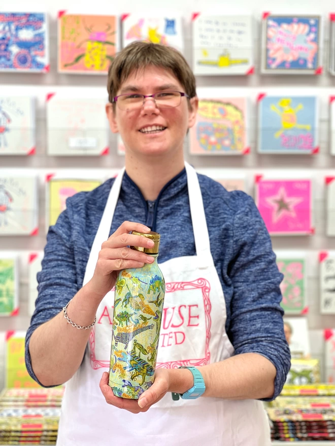 Happy artist holding dinosaurs sustainable insulated charity water bottle in blues & yellows