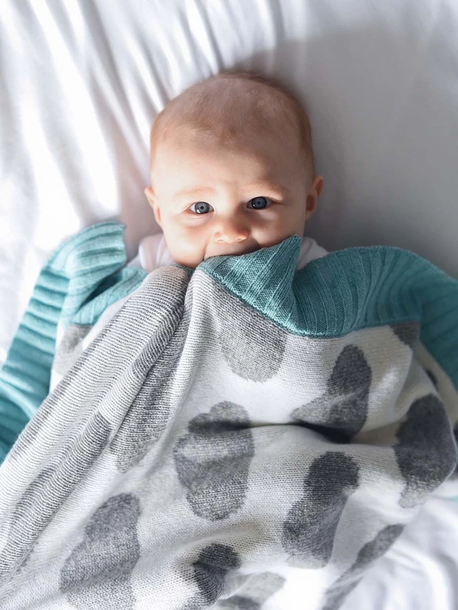 Baby laid on a bed, wrapped in a blanket with a cloud design,  gazing straight at the camera with big blue eyes.