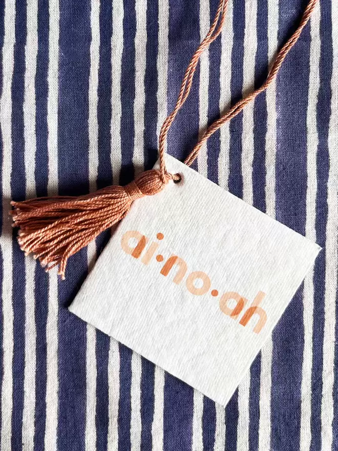 Detail of recycled swing tag featuring ainhoa logo and dusty pink tassel and hanging loop
