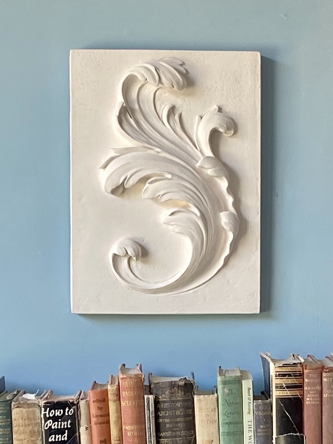 Plaster bas-relief wall plaque with acanthus leaf design and books underneath