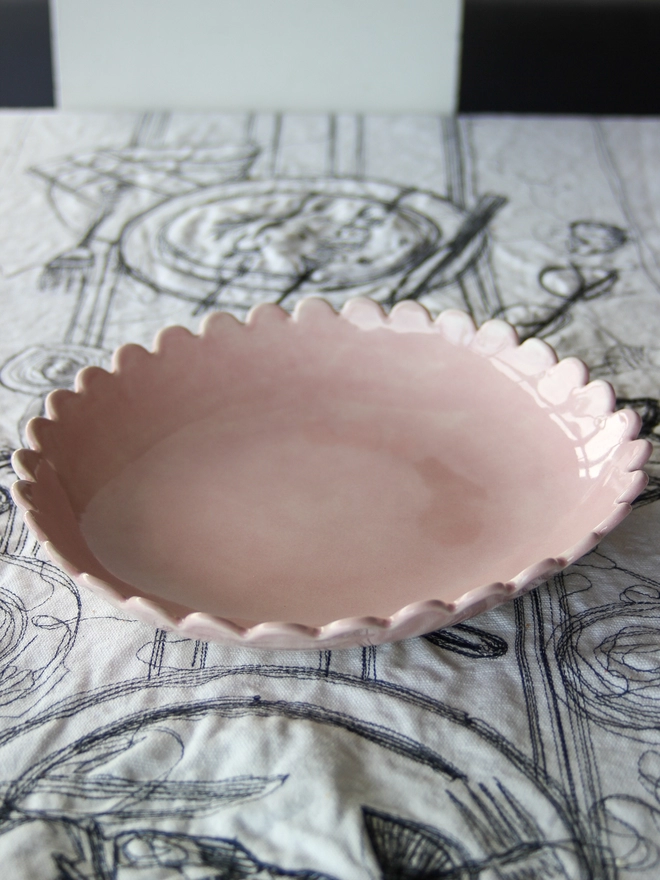 a pink scalloped edge pasta or serving bowl, handmade in UK on black and white tablecloth