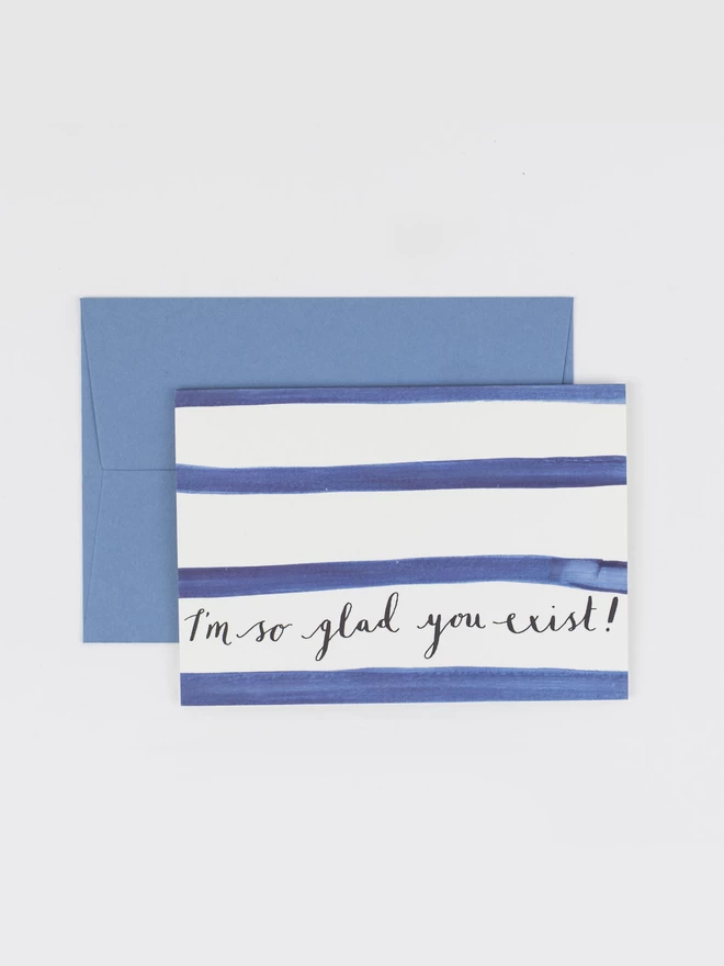 A card featuring breton stripes and hand lettered text in calligraphy that reads "I'm so glad you exist"