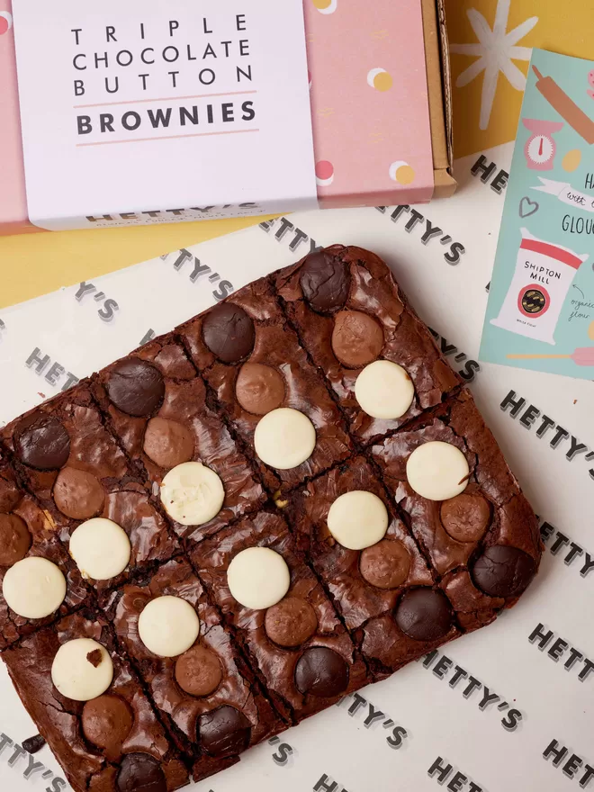 Ten slices of triple chocolate brownies in a flat lay with branded box and postcard