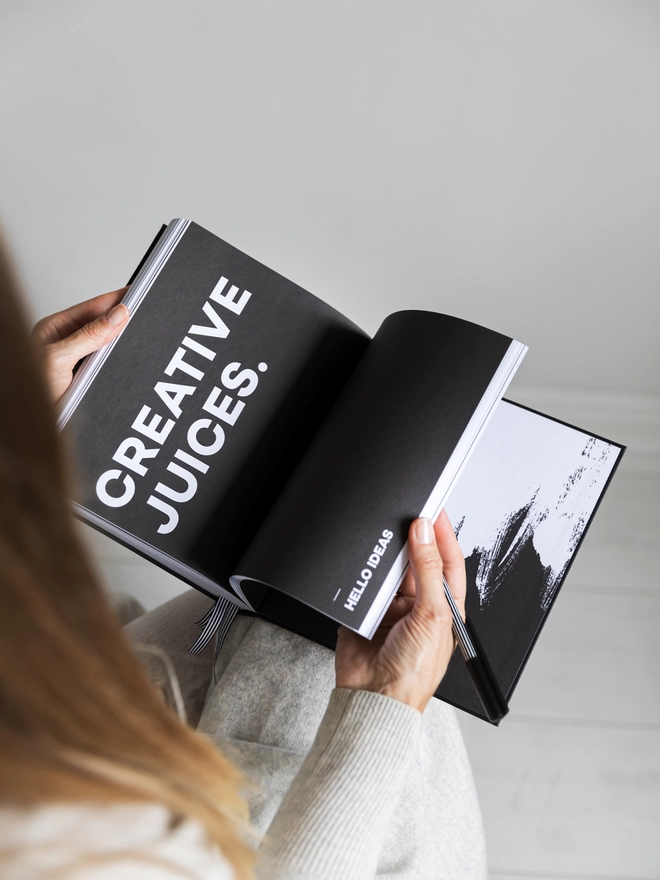 Lady flicking through a HELLO TIME planner onto a black quote page reading 'Creative Juices'