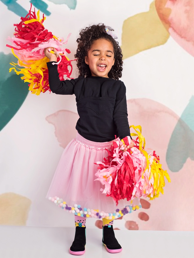 Young girl holding pom poms while wearing a pink pom pom tutu