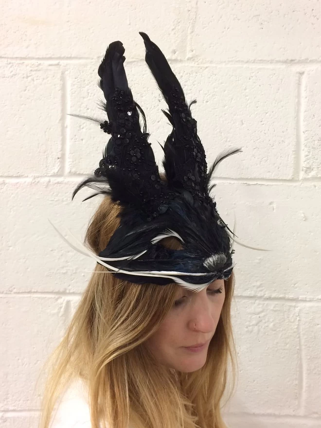A woman wearing a luxury black embellished rabbit party mask perched atop her head as a headdress