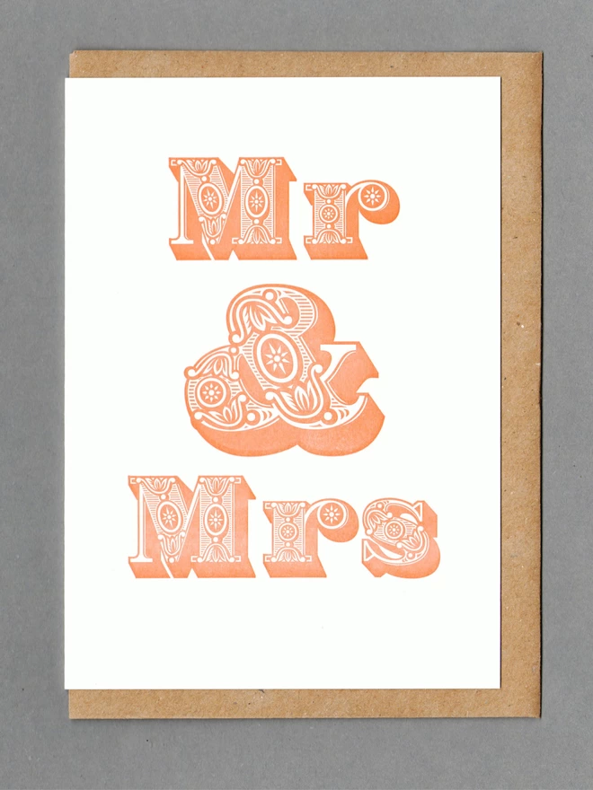 White card with orange text reading 'Mr & Mrs' with a kraft envelope behind it
