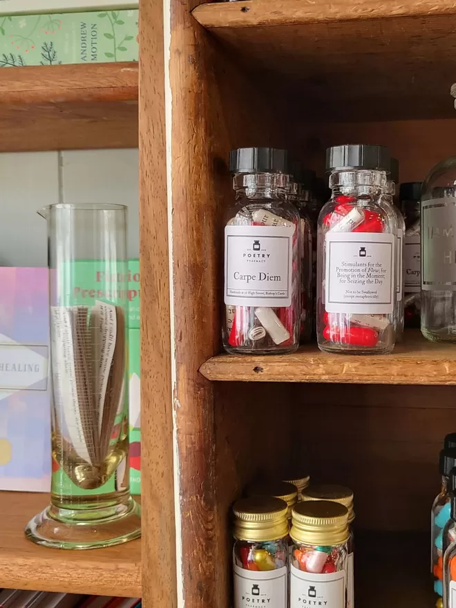 A shelf of colourful poetry pills at the poetry pharmacy, next to a glass flask of poetry quotes