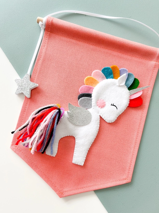A white unicorn on a coral coloured canvas fabric