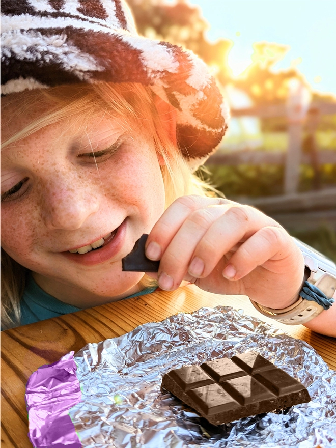 Young child opening purple foil wrapped charity dark chocolate bar with sea salt cinnamon & vanilla