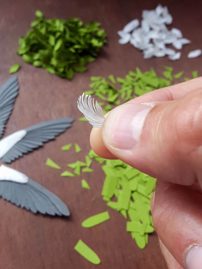 Small paper feather in hand over paper wings