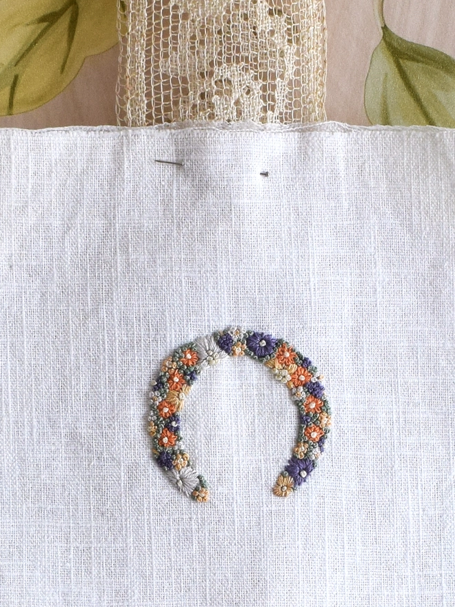 An embroidered Heart of Golden Yellows and Bright Orange Blossoms with Green French Knot grass background.  Pinned to a length of vintage lace, with ends pointing down to allow Luck to flow over all who pass by.