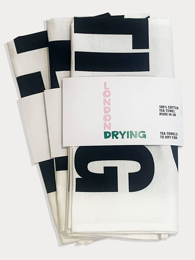 A few white tea towels with black text folded in London Drying branded "belly wrap" to show packaging
