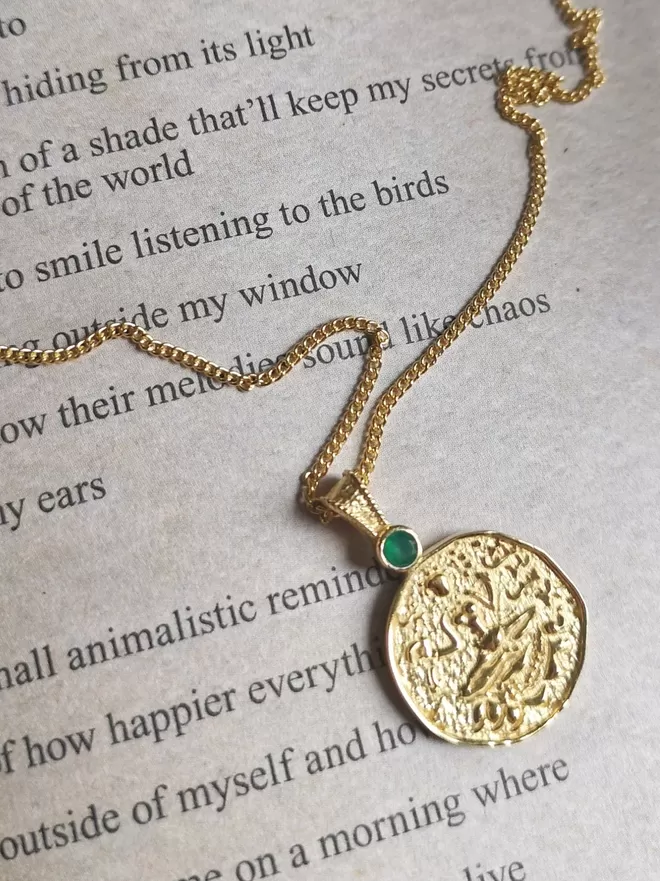 Lakshmi coin pendant by Loft & Daughter on an open book