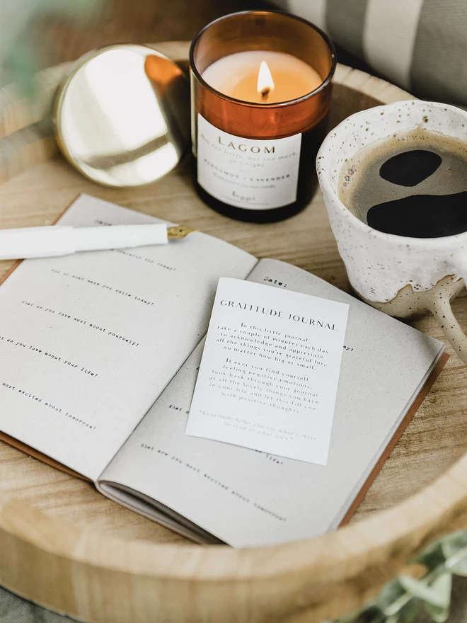 open gratitude journal beside a lit candle and a cup of black coffee