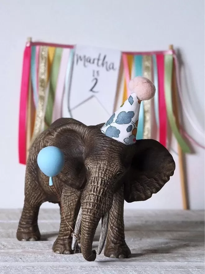 Elephant seen with a blue party hat in front of a birthday sign.