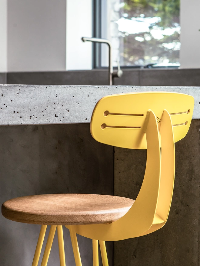 set of four bright yelhairpin leg bar chair with with oak seat and bright yellow legs and back, pushed up against a polished concrete kitchen island