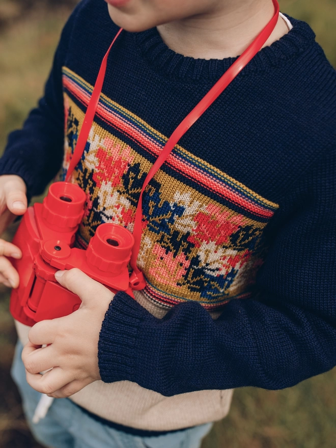 A young boy holding a pair of red binoculars, wearing The Faraway Gang's The 'Adventurer' Knitted Jumper.