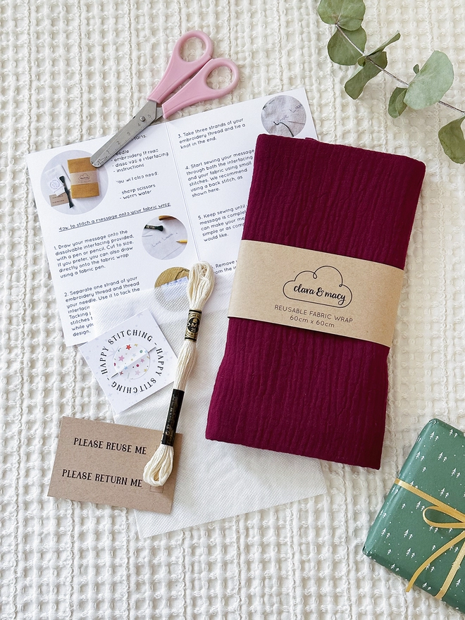 A fabric wrap is folded with a sleeve around it and an embroidery kit lays beside.