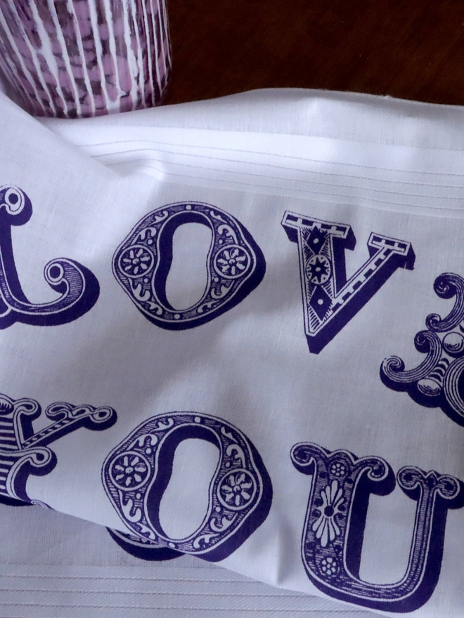Detail close-up of A Mr.PS Love Uou Lots hankie printed in violet in front of a handmade glass vase