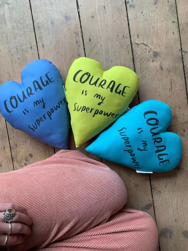Courage heart plushies seen in green and blue on a wooden floor