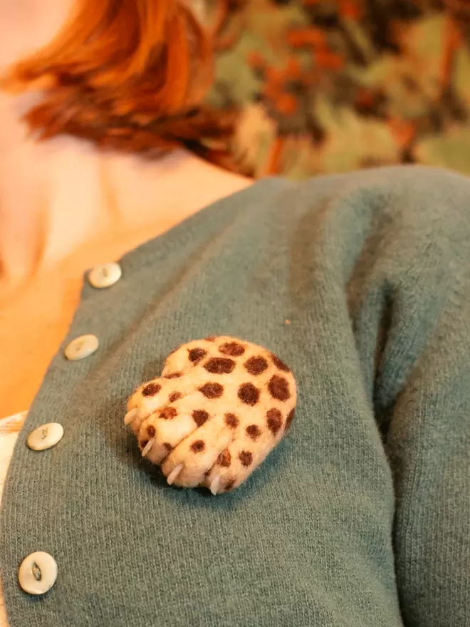 A needle-felted Lucky Leopard being worn on a green cardigan