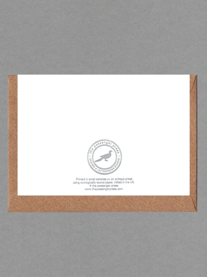 Back of white card with silver text on it with a brown envelope behind