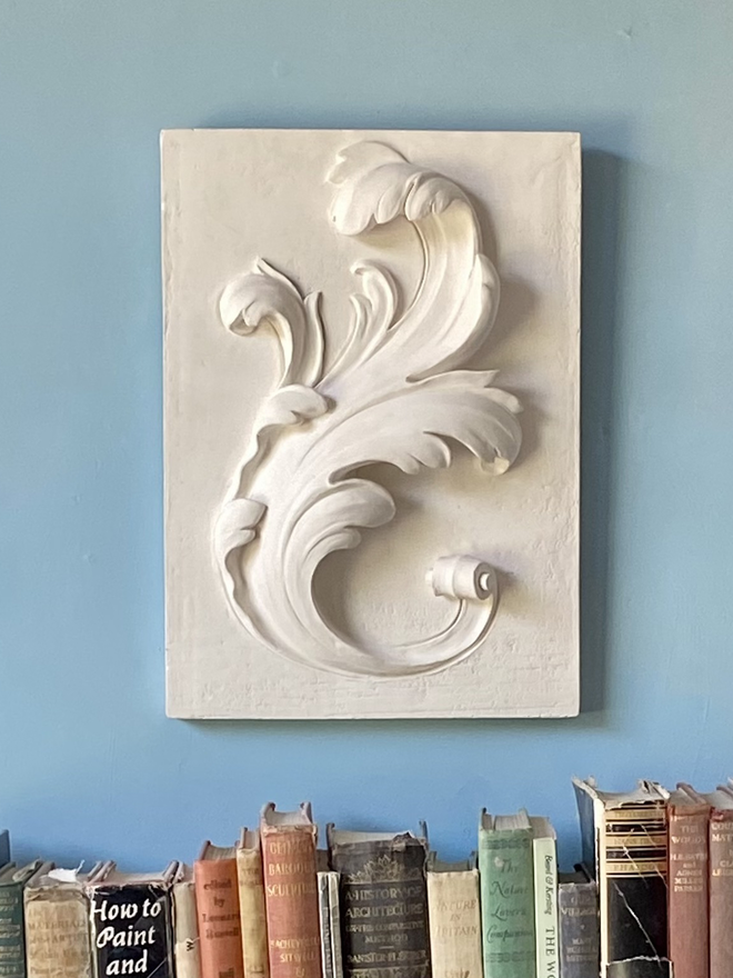 Plaster bas-relief wall sculpture with raffle leaf design and books underneath