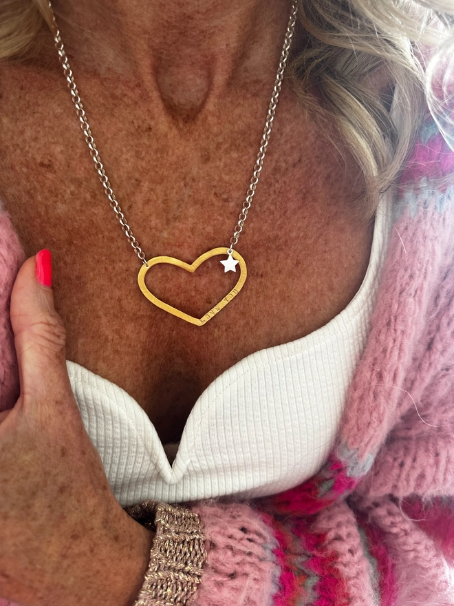 model wears large gold open heart charm on a sterling silver chain with a small silver star charm