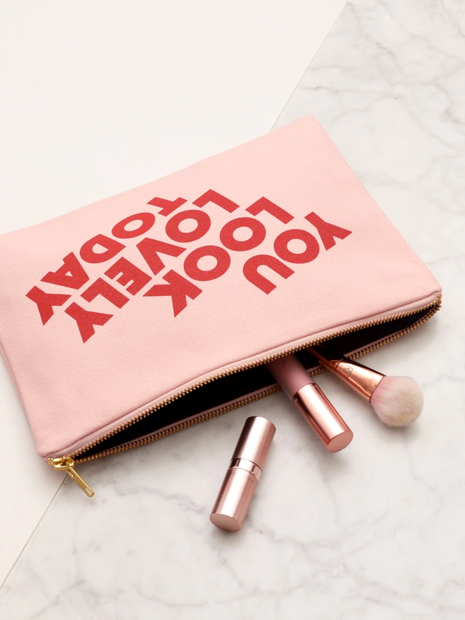 a blush pink canvas zip pouch with the words you look lovely today with makeup spilling out