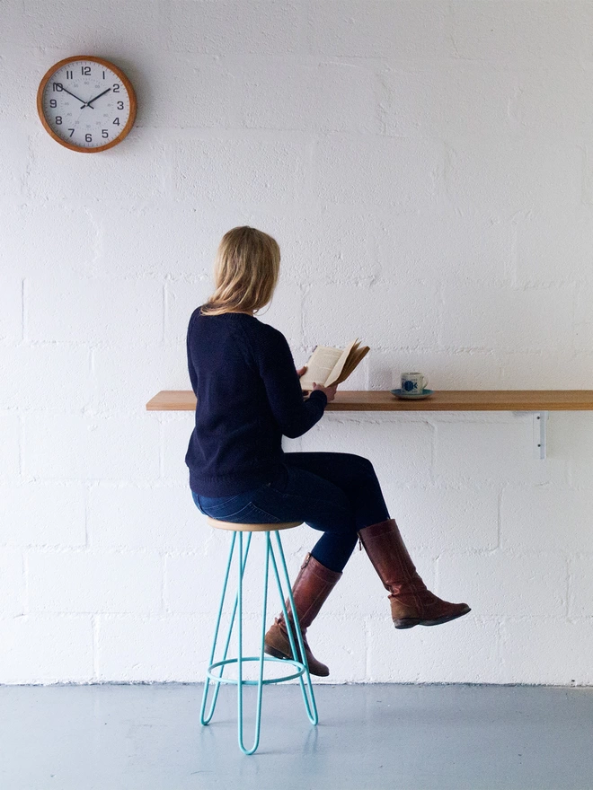 woman sat reading on a bar stool with turquoise hairpin legs